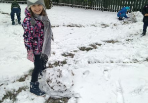 Roześmiana dziewczynka stoi obok śnieżnej kuli